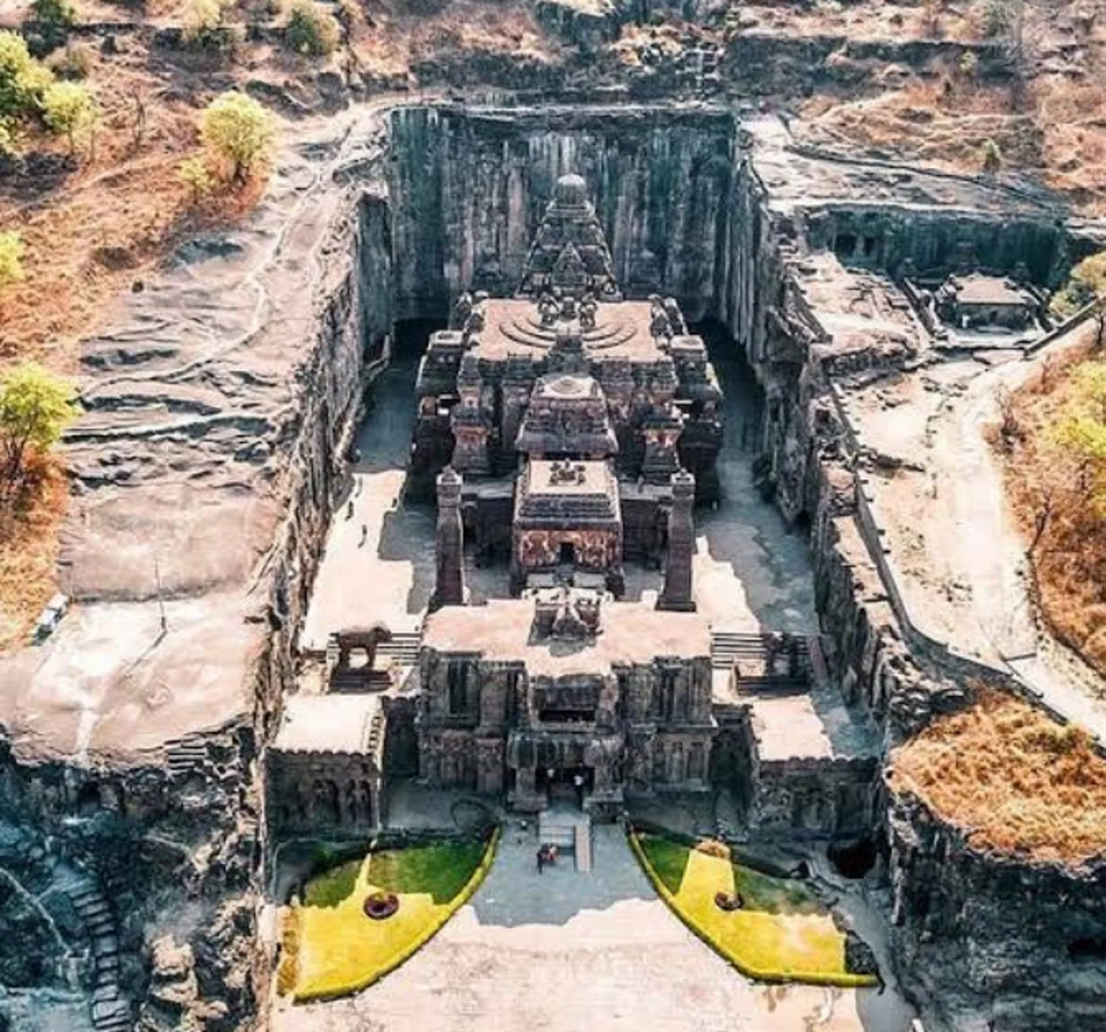 Aerial drone view of the Kailasa Temple at Ellora (Cave 16) — the entire temple complex carved top-down out of the living basalt cliff, seen from above. Photograph.